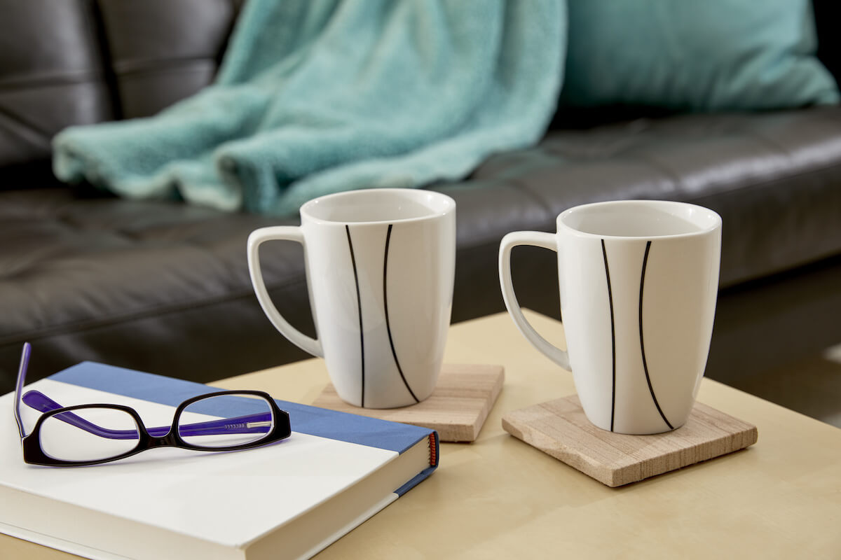 2 mugs on coasters beside a book and eyeglasses