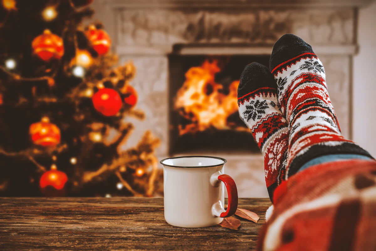 Person wearing Christmas-themed socks relaxing by a fireplace