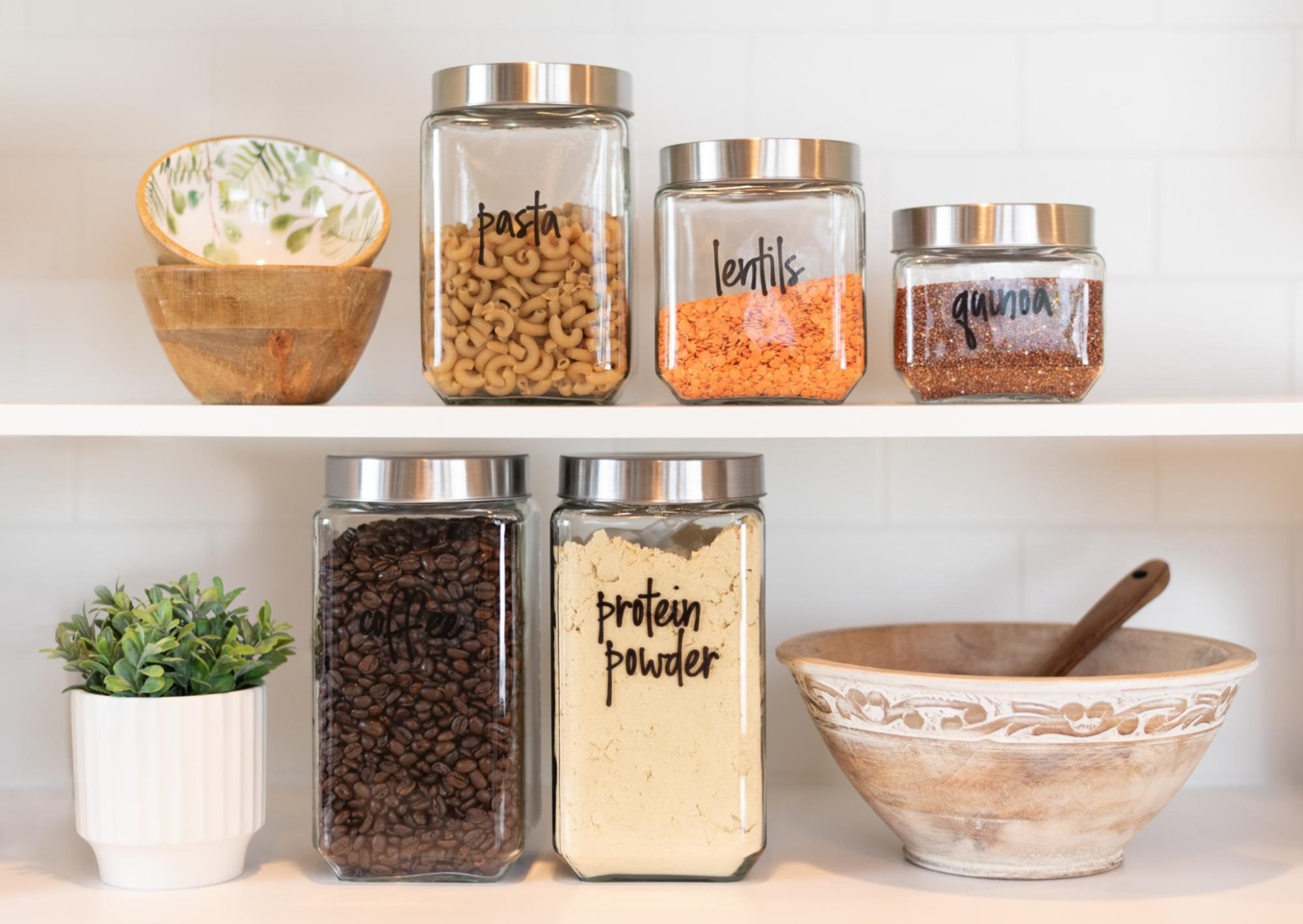 Dry food ingredients in glass jars on a white kitchen shelf