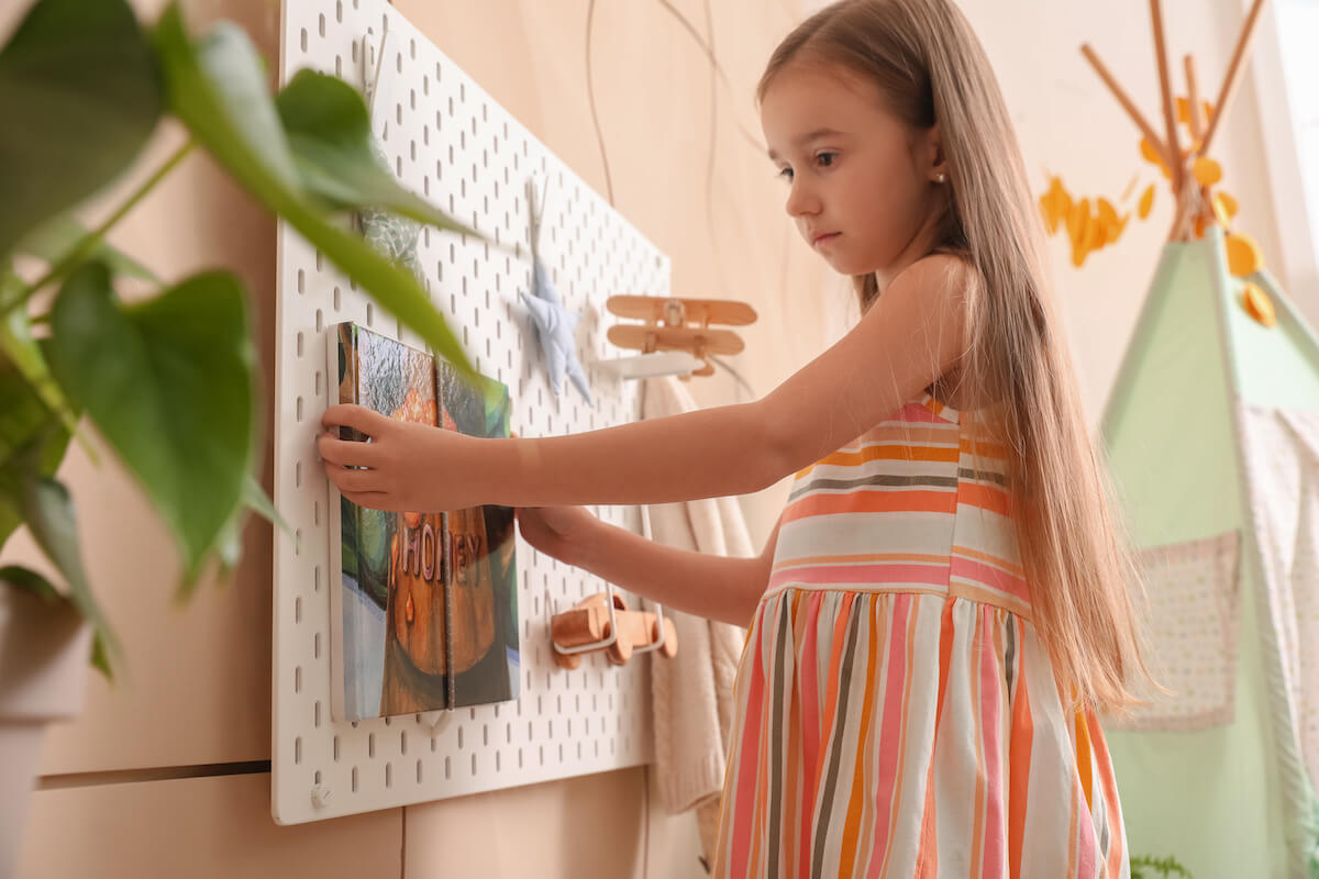 Little girl hanging a painting onto a peg board