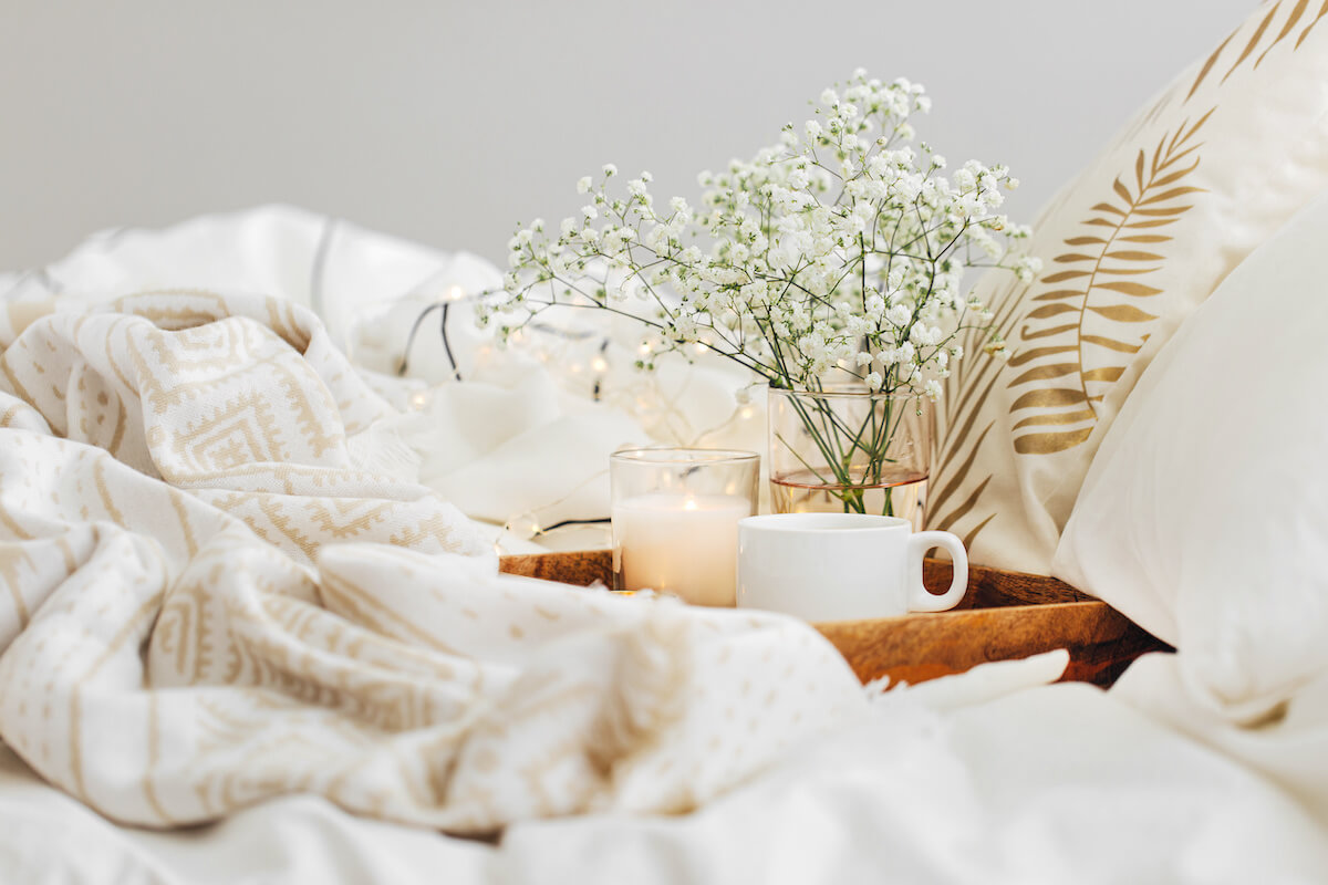 Wooden tray with flowers, a candle and cup of coffee on a bed